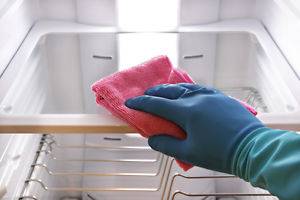 woman's hand with gloves on cleaning interior of refrigerator